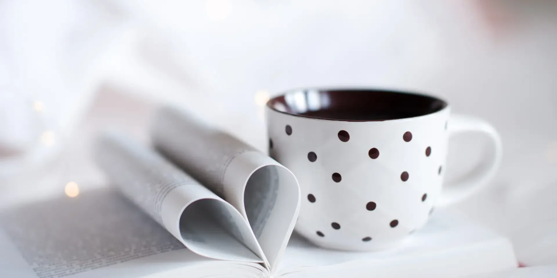 cup-hot-tea-stay-open-paper-book-with-folded-pages-heart-shape-glow-lights-bed-close-up-home-cozy-atmosphere